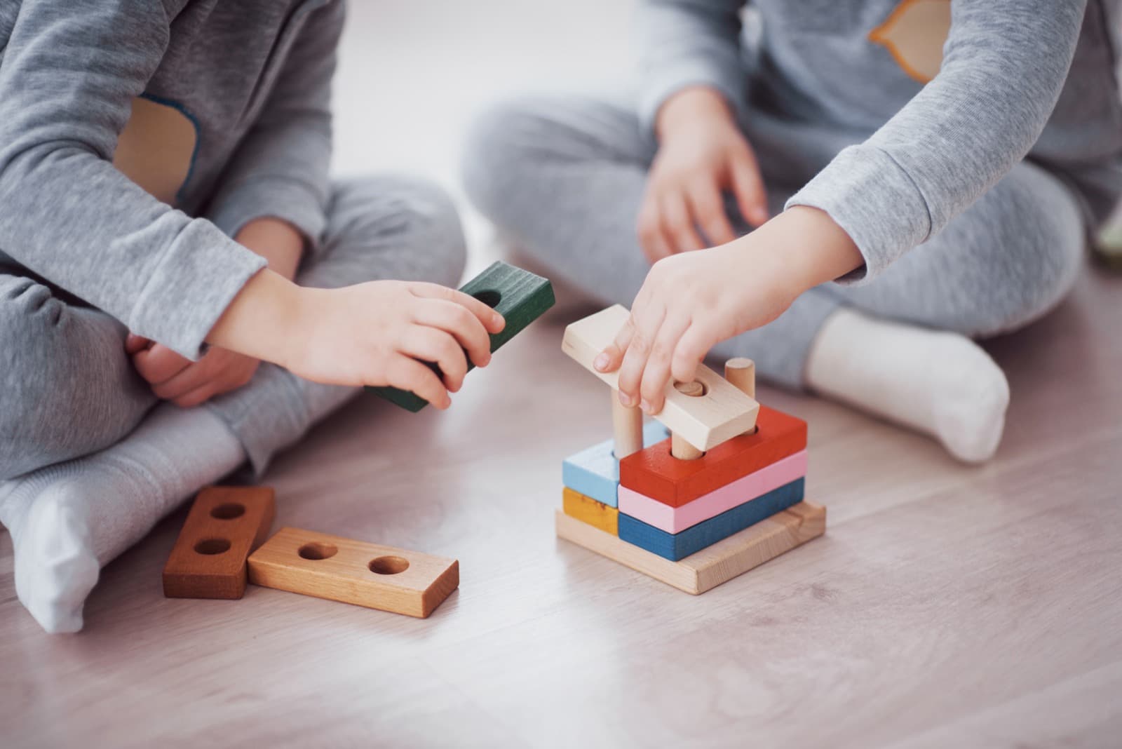 Zwei Kinder spielen gemeinsam mit bunten Holzbausteinen auf dem Boden